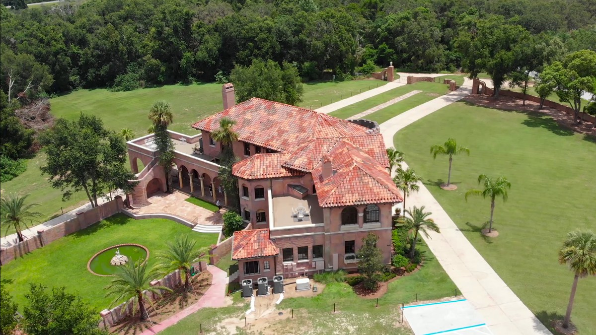 The restored 1925 mansion from the air, its tiled roofs, walled courtyard, palm drive and lawn.